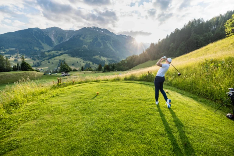 Golferin schlägt auf dem Golfplatz Klosters im Abendlicht ab