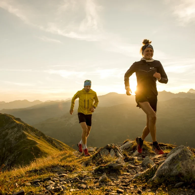 Zwei Trailrunner laufen bei Sonnenaufgang über einen Bergkamm