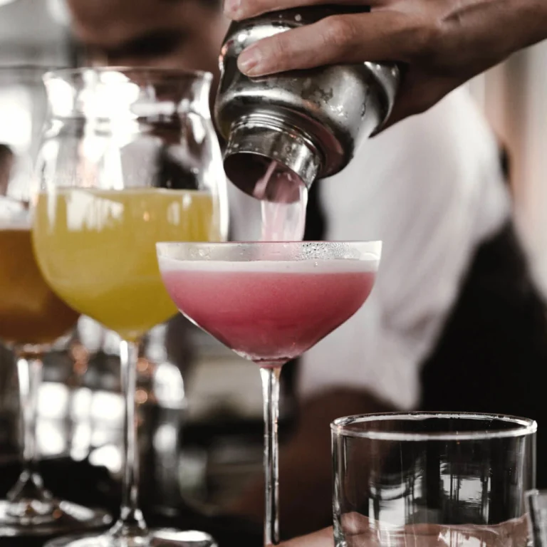 Barkeeper giesst einen rosa Cocktail aus dem Shaker in ein Coupe-Glas