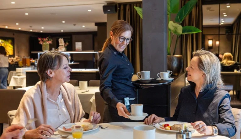Servicemitarbeiterin serviert zwei Gästen Kaffee im Restaurant